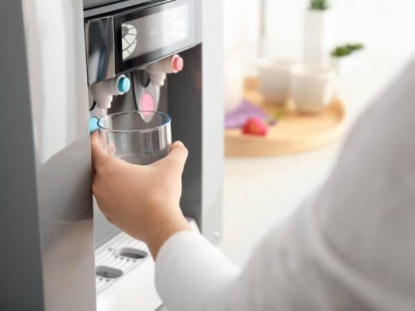 Persona riempie bicchiere d'acqua da un depuratore domestico