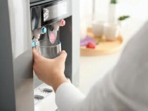 Persona riempie bicchiere d'acqua da un depuratore domestico